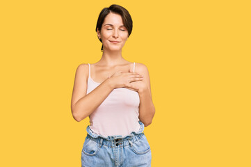 Young brunette woman with short hair wearing casual summer clothes smiling with hands on chest with closed eyes and grateful gesture on face. health concept.