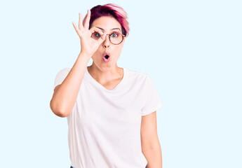 Young beautiful woman with pink hair wearing casual clothes and glasses doing ok gesture shocked with surprised face, eye looking through fingers. unbelieving expression.