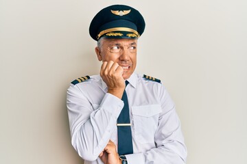 Handsome middle age mature man wearing airplane pilot uniform looking stressed and nervous with hands on mouth biting nails. anxiety problem. © Krakenimages.com