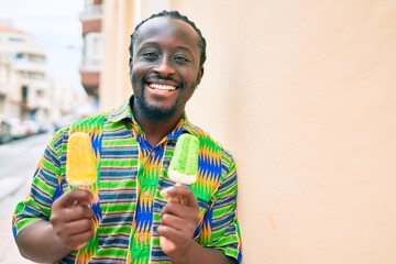 Young african american man eating ice cream leaning on the wall at street of city.