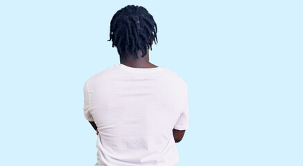 Young african american man with braids wearing casual white tshirt standing backwards looking away...