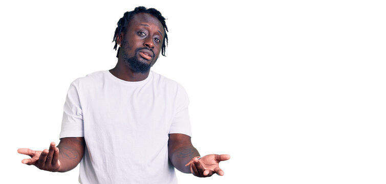 Young african american man with braids wearing casual white tshirt clueless and confused with open arms, no idea concept.