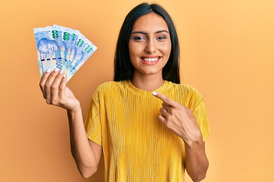 Young brunette woman holding south african 100 rand banknotes smiling happy pointing with hand and finger