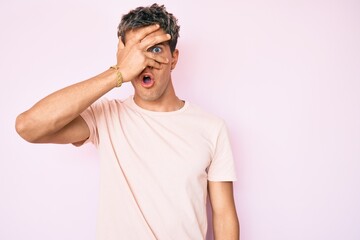 Young handsome man wearing casual clothes peeking in shock covering face and eyes with hand, looking through fingers afraid