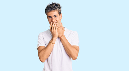 Young handsome man wearing casual white tshirt laughing and embarrassed giggle covering mouth with...