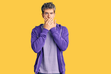 Young handsome man wearing casual purple sweatshirt shocked covering mouth with hands for mistake. secret concept.