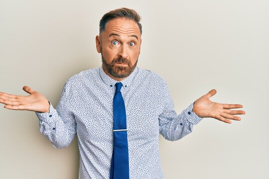 Handsome middle age man wearing business shirt and tie clueless and confused expression with arms and hands raised. doubt concept.