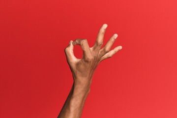 Hand of hispanic man over red isolated background gesturing approval expression doing okay symbol with fingers