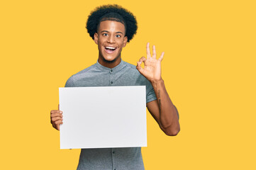 African american man with afro hair holding blank empty banner doing ok sign with fingers, smiling friendly gesturing excellent symbol