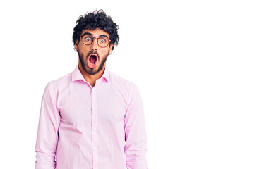 Handsome young man with curly hair and bear wearing business clothes afraid and shocked with surprise expression, fear and excited face.