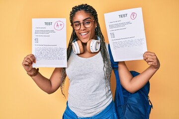 Young african american woman with braids showing failed and passed exam winking looking at the...