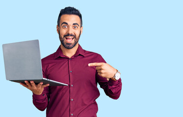 Young hispanic man holding laptop smiling happy pointing with hand and finger