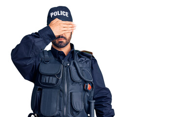 Young hispanic man wearing police uniform covering eyes with hand, looking serious and sad. sightless, hiding and rejection concept