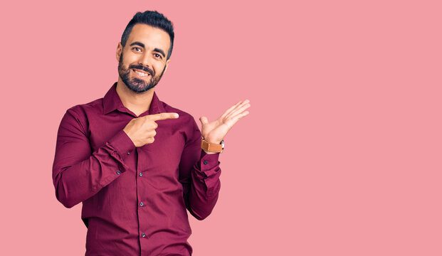 Young hispanic man wearing casual clothes amazed and smiling to the camera while presenting with hand and pointing with finger.