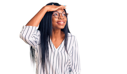 Young african american woman wearing casual clothes and glasses very happy and smiling looking far away with hand over head. searching concept.