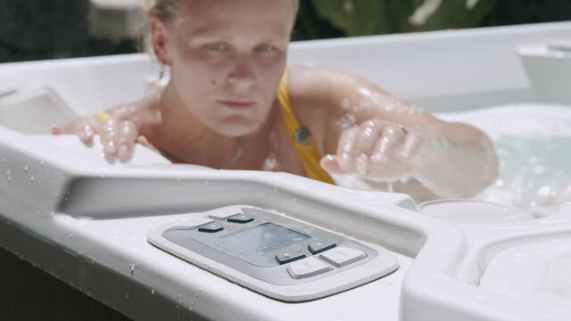A young woman relaxing in bath, pushing some buttons on a control panel