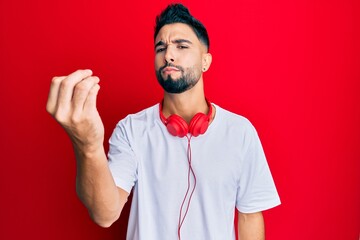 Young man with beard listening to music using headphones doing italian gesture with hand and fingers confident expression
