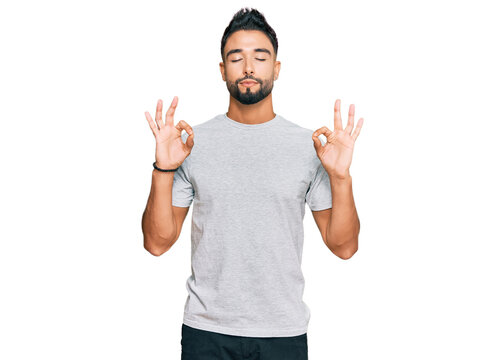 Young man with beard wearing casual grey tshirt relax and smiling with eyes closed doing meditation gesture with fingers. yoga concept.