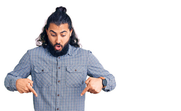 Young arab man wearing casual clothes pointing down with fingers showing advertisement, surprised face and open mouth