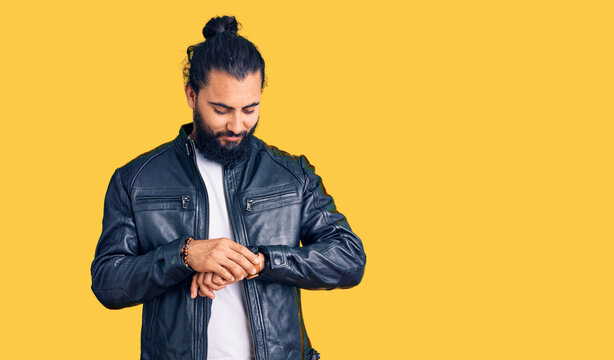 Young arab man wearing casual leather jacket checking the time on wrist watch, relaxed and confident