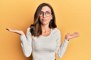 Young brunette woman wearing casual clothes and glasses clueless and confused with open arms, no...