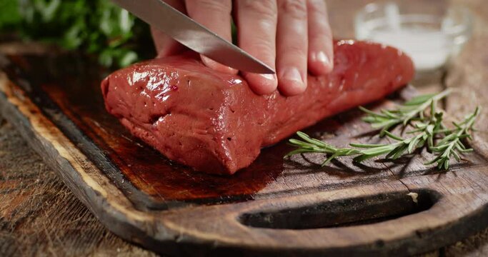 Slicing the raw liver on a wooden cutting board. 