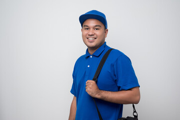 Young smiling asian delivery man in blue uniform holding messenger bag standing on isolated white...