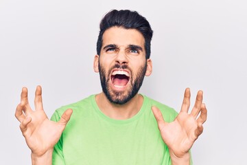 Young handsome man with beard wearing casual t-shirt crazy and mad shouting and yelling with aggressive expression and arms raised. frustration concept.