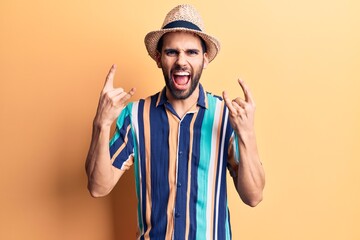 Young handsome man with beard wearing summer hat and shirt shouting with crazy expression doing rock symbol with hands up. music star. heavy concept.