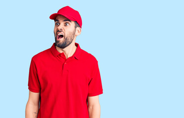 Young handsome man with beard wearing delivery uniform angry and mad screaming frustrated and furious, shouting with anger. rage and aggressive concept.