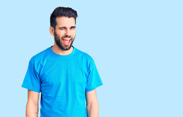 Young handsome man with beard wearing casual t-shirt winking looking at the camera with sexy expression, cheerful and happy face.