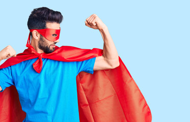 Young handsome man with beard wearing super hero costume showing arms muscles smiling proud....