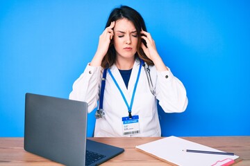 Young beautiful brunette woman wearing doctor uniform working at the clinic with hand on head, headache because stress. suffering migraine.