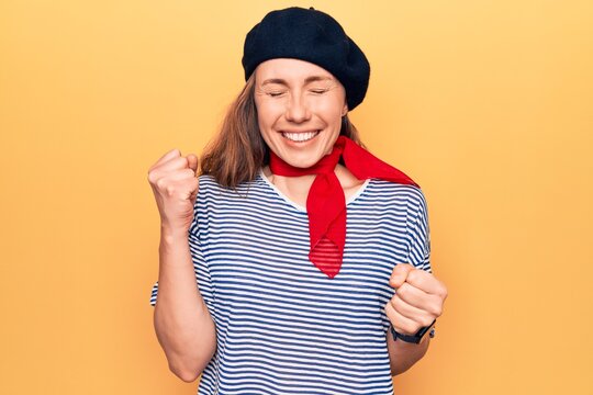 Young beautiful blonde woman wearing french fashion style with scarf and beret celebrating surprised and amazed for success with arms raised and eyes closed