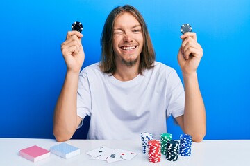 Handsome caucasian man with long hair playing poker holding casino chips winking looking at the...