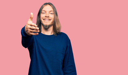 Handsome caucasian man with long hair wearing casual winter sweater smiling friendly offering handshake as greeting and welcoming. successful business.