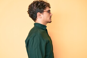 Obraz premium Young caucasian man with curly hair wearing casual clothes and glasses looking to side, relax profile pose with natural face with confident smile.