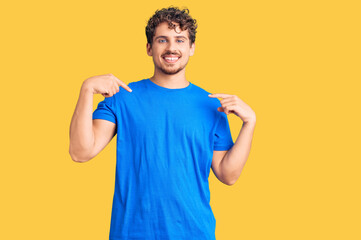 Young handsome man with curly hair wearing casual clothes looking confident with smile on face, pointing oneself with fingers proud and happy.
