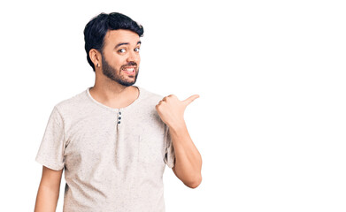 Young hispanic man wearing casual clothes smiling with happy face looking and pointing to the side with thumb up.