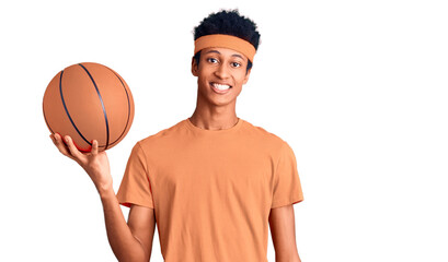 Obraz premium Young african american man holding basketball ball looking positive and happy standing and smiling with a confident smile showing teeth