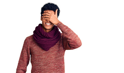 Young african american man wearing casual winter sweater and scarf smiling and laughing with hand on face covering eyes for surprise. blind concept.