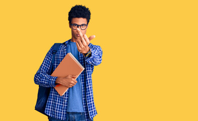 Young african american man wearing student backpack holding book showing middle finger, impolite...