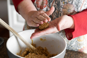 Middle aged women preparing anzac biscuit ball in home kitchen.