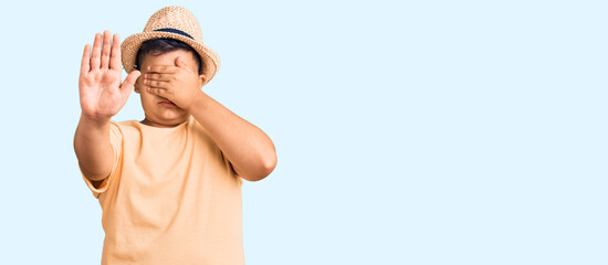 Little boy kid wearing summer hat and hawaiian swimsuit covering eyes with hands and doing stop gesture with sad and fear expression. embarrassed and negative concept. © Krakenimages.com