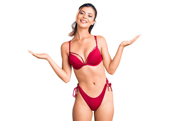 Young beautiful woman wearing bikini smiling showing both hands open palms, presenting and...
