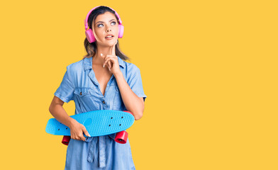 Young beautiful woman wearing headphones and holding skate serious face thinking about question...