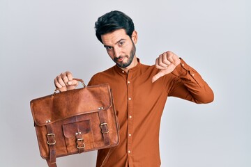 Young hispanic man wearing leather bag with angry face, negative sign showing dislike with thumbs...