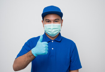 Fototapeta na wymiar Blue delivery asian man wearing protection mask and medical rubber gloves standing showing thumbs up on isolated white background safety deliver concept.