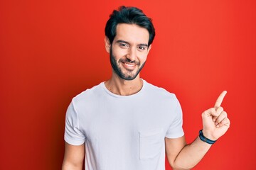 Young hispanic man wearing casual white tshirt with a big smile on face, pointing with hand finger to the side looking at the camera.