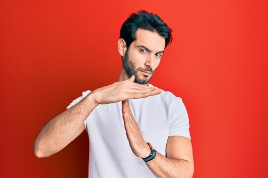 Young hispanic man wearing casual white tshirt doing time out gesture with hands, frustrated and serious face